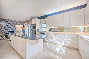 A modern kitchen with white cabinetry, a central island, and a backsplash with a floral pattern. - Lanai & Pool: Elegant Villa in Winter Haven! (Winter Haven)