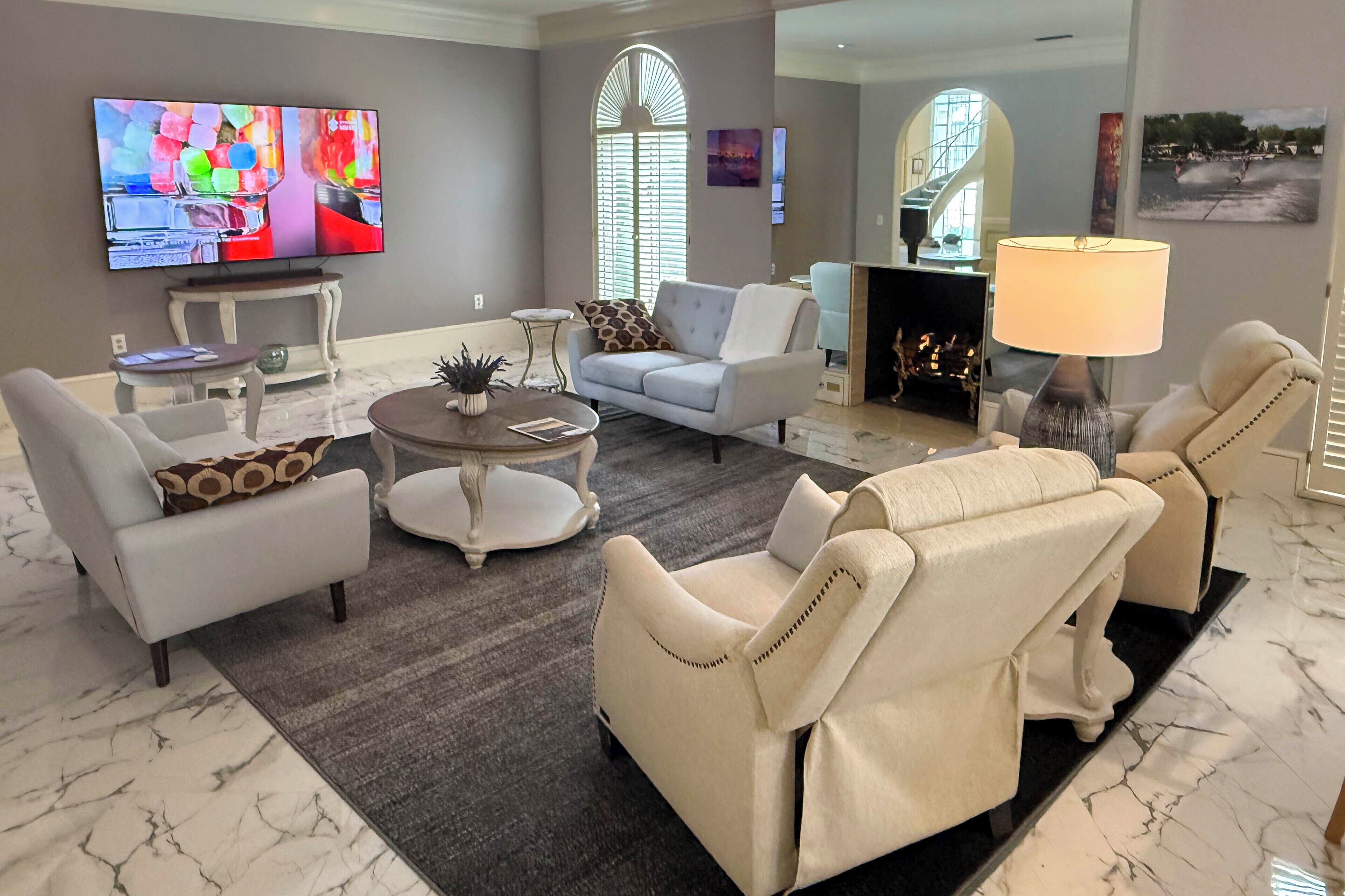 A spacious living room with a flat-screen TV, comfortable seating, a fireplace, and a large window.