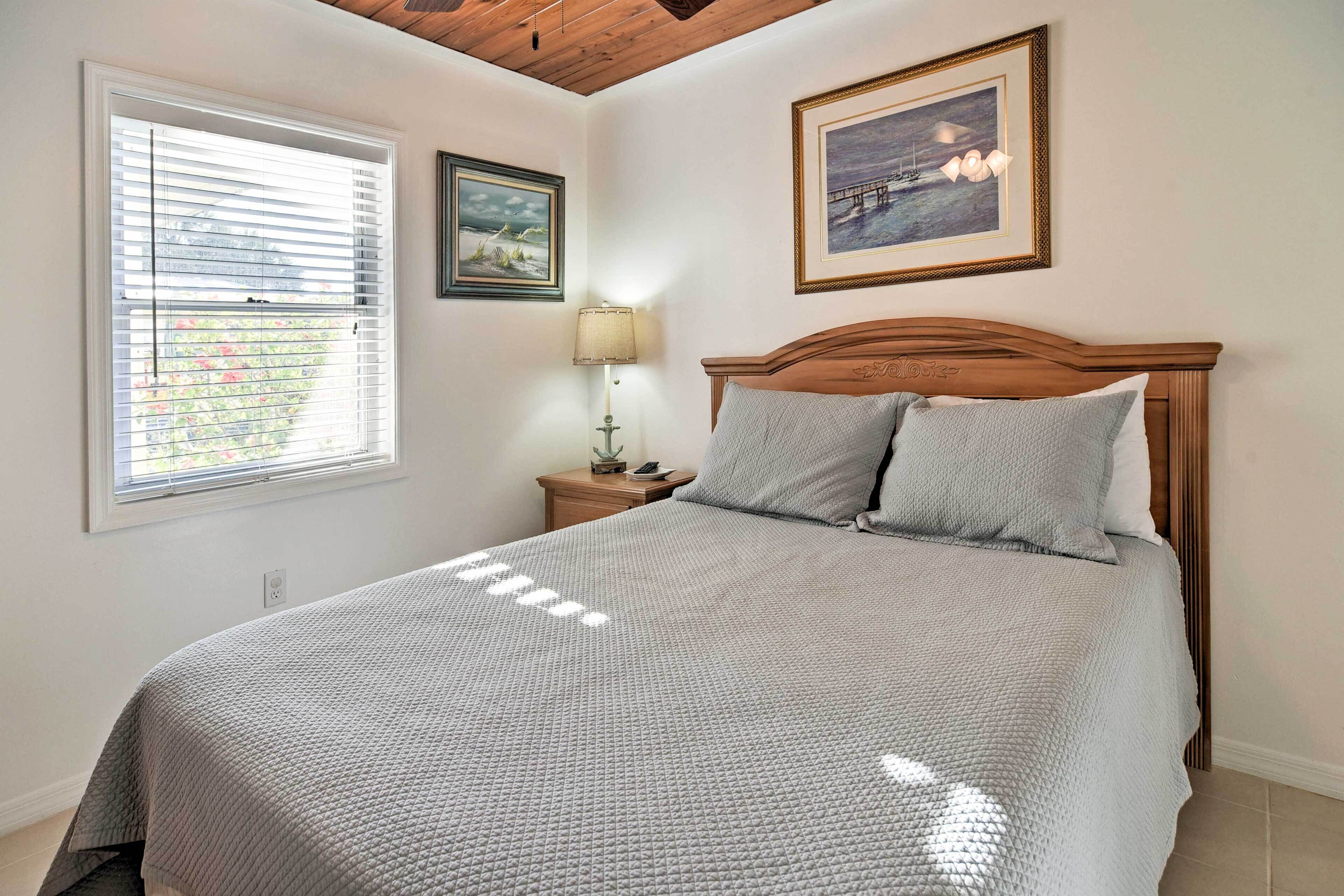 A bedroom with a large bed, a wooden headboard, a nightstand with a lamp, and two framed pictures on the wall.