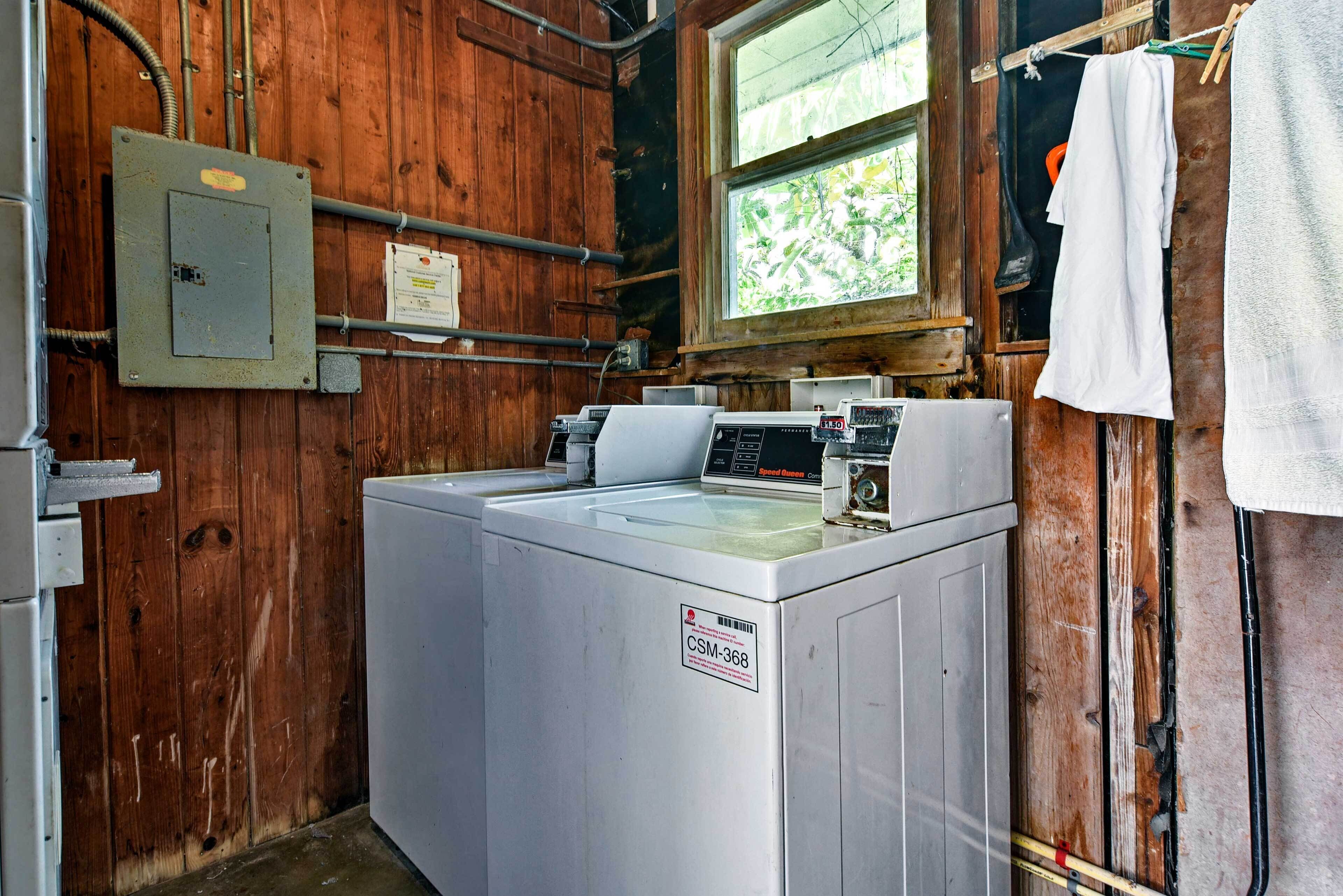A laundry room with a front-loading washer and dryer, wooden walls, a window, and visible plumbing.