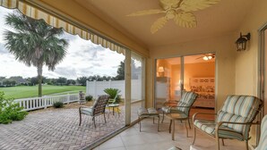 A covered patio with striped chairs and a view of a lawn and palm tree. - The Villages Home on Golf Course Near Lake Sumter! (The Villages)