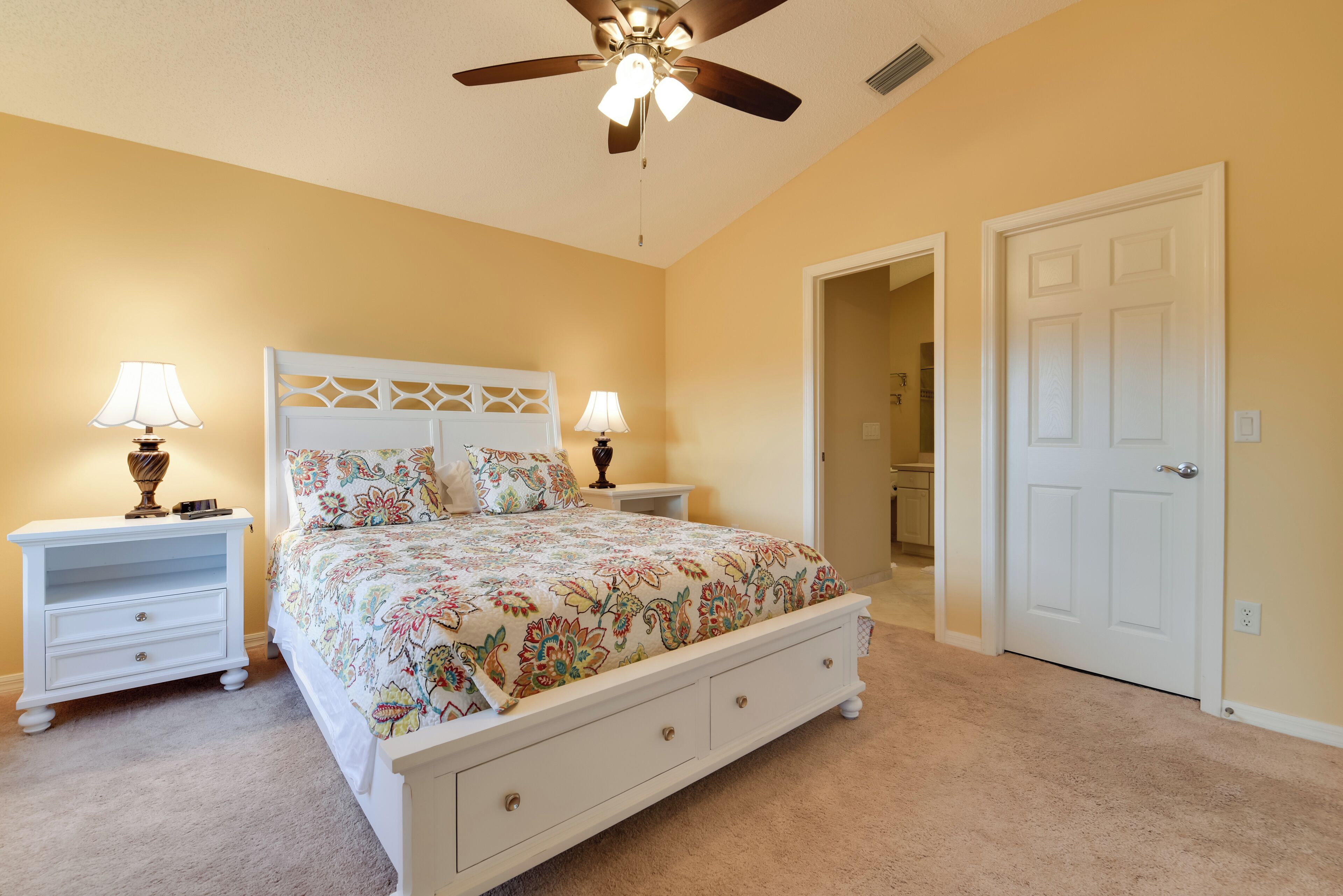 A bedroom with a bed, two bedside tables, a ceiling fan, and a door.