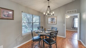 A dining area with a round table, six chairs, and a chandelier. There are two windows with blinds, a ceiling vent, and framed artwork on the walls. - Deltona Retreat w/ Yard + Grill: Pets Welcome! (Deltona)