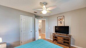 A bedroom with a bed, a ceiling fan, a TV on a wooden stand, and a door leading to another room. - Deltona Retreat w/ Yard + Grill: Pets Welcome! (Deltona)