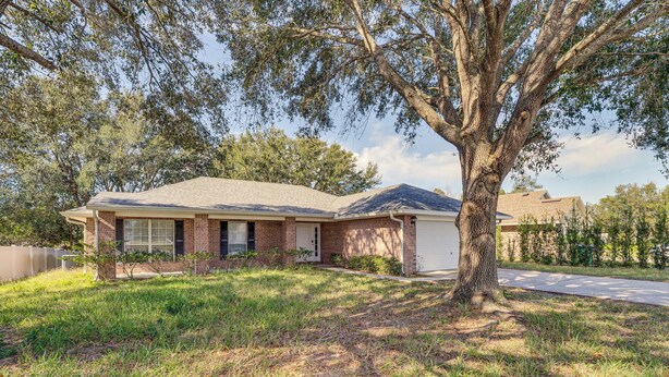 A single-story house with a brick facade, a front porch, and a large tree in front. - Deltona Retreat w/ Yard + Grill: Pets Welcome! (Deltona)