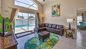 Ein geräumiges Wohnzimmer mit einer großen Eckcouch, einem Couchtisch und einem Deckenventilator. Ein großes Fenster sorgt für natürliches Licht und bietet Blick auf einen Swimmingpool.