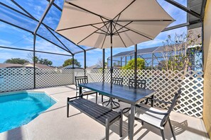 An outdoor patio with a pool, a table with chairs, and a large umbrella.