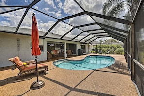 A covered outdoor swimming pool with lounge chairs and an umbrella, surrounded by a metal framework. - Pet-friendly Fort Myers Home w/ Patio & Grill! (North Fort Myers)