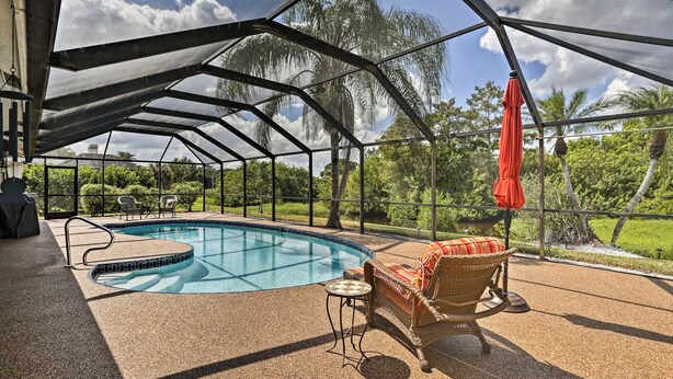 A covered outdoor swimming pool with a view of palm trees and a grassy area. - Pet-friendly Fort Myers Home w/ Patio & Grill! (North Fort Myers)