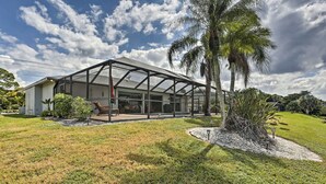 A modern house with a glass-enclosed patio, surrounded by a well-maintained lawn and palm trees. - Pet-friendly Fort Myers Home w/ Patio & Grill! (North Fort Myers)