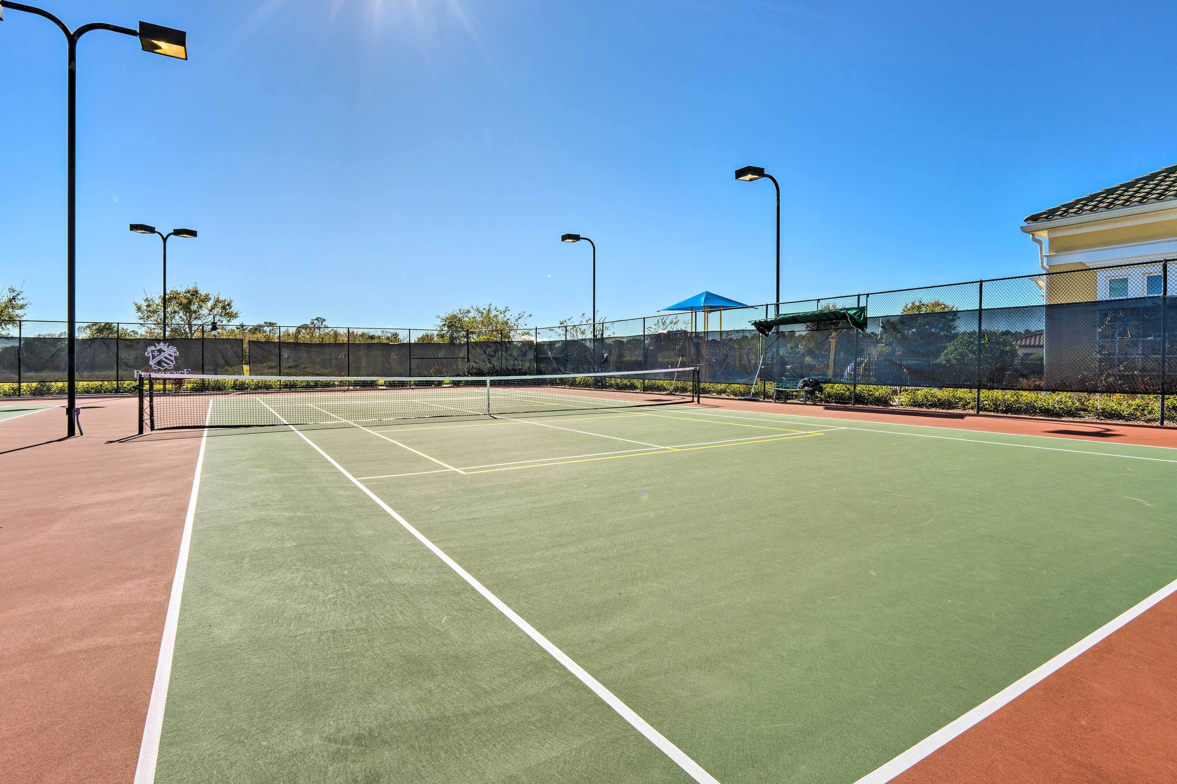 A tennis court with a net, surrounded by a fence, and street lamps.