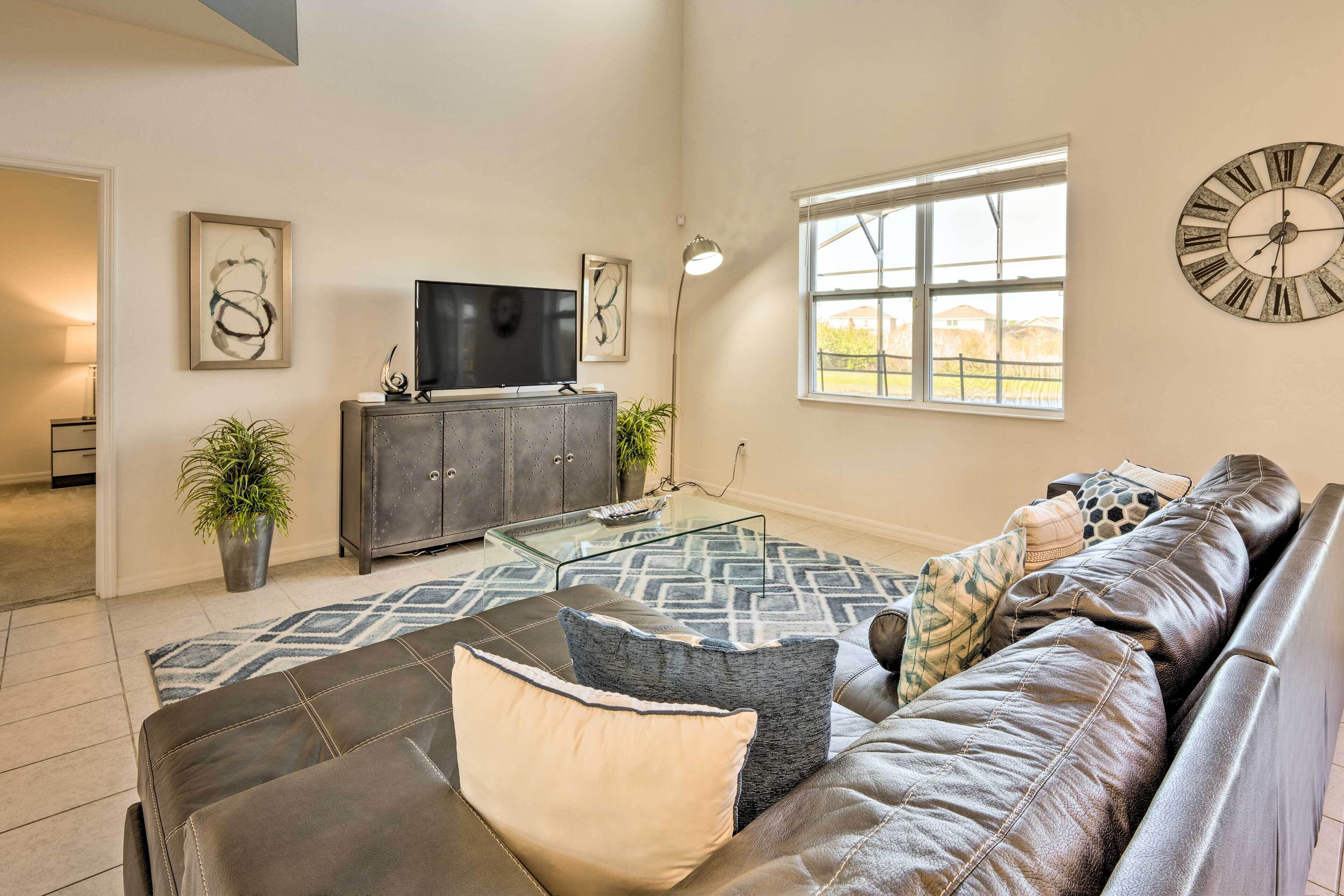 A living room with a leather sofa, a glass coffee table, a television on a cabinet, and a large window with a view.