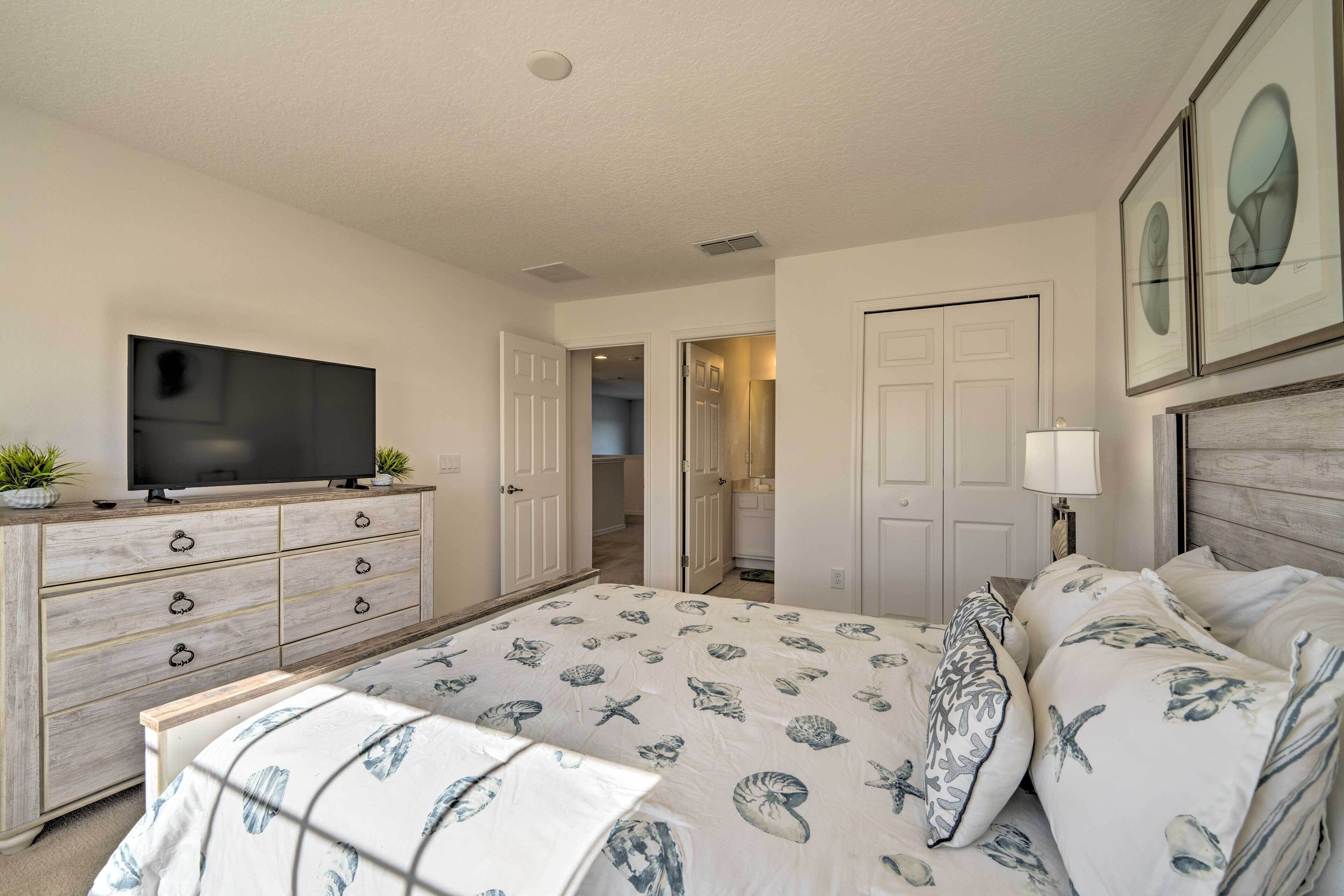 A bedroom with a bed, dresser, television, and framed artwork on the wall.