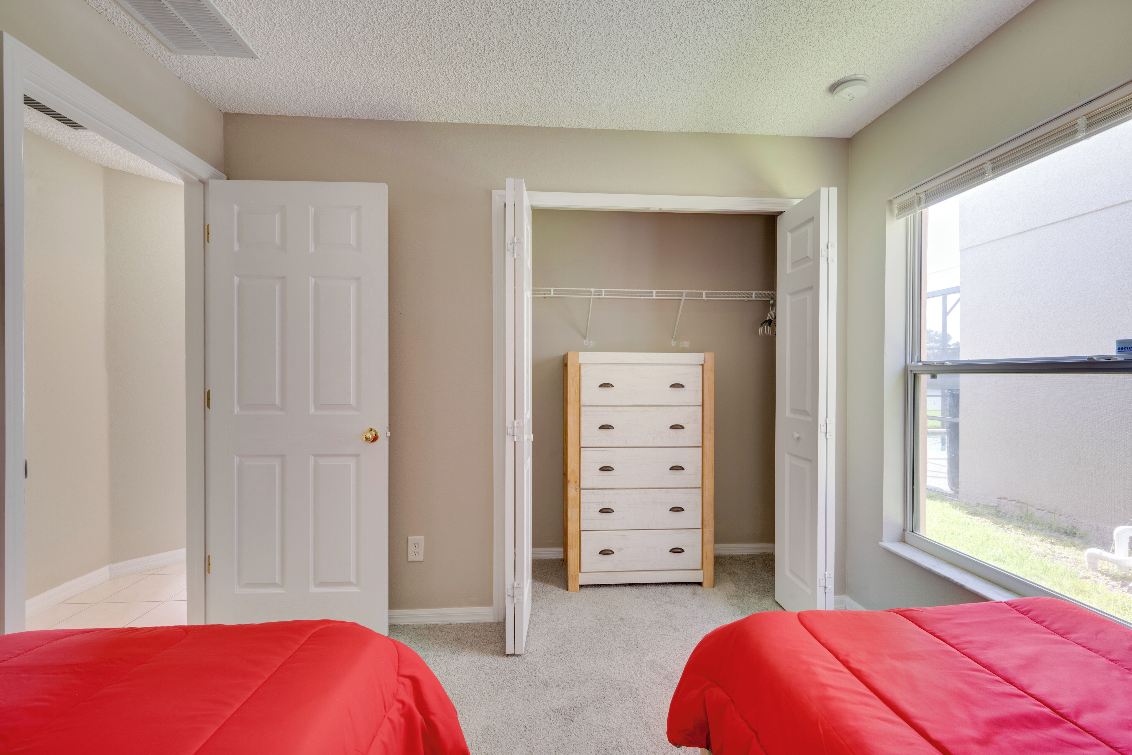 A bedroom with two beds, a closet with a wooden dresser, and a window with a view of the outside.