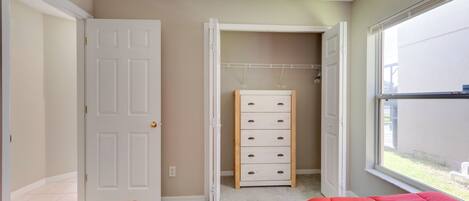 A bedroom with two beds, a closet with a wooden dresser, and a window with a view of the outside.