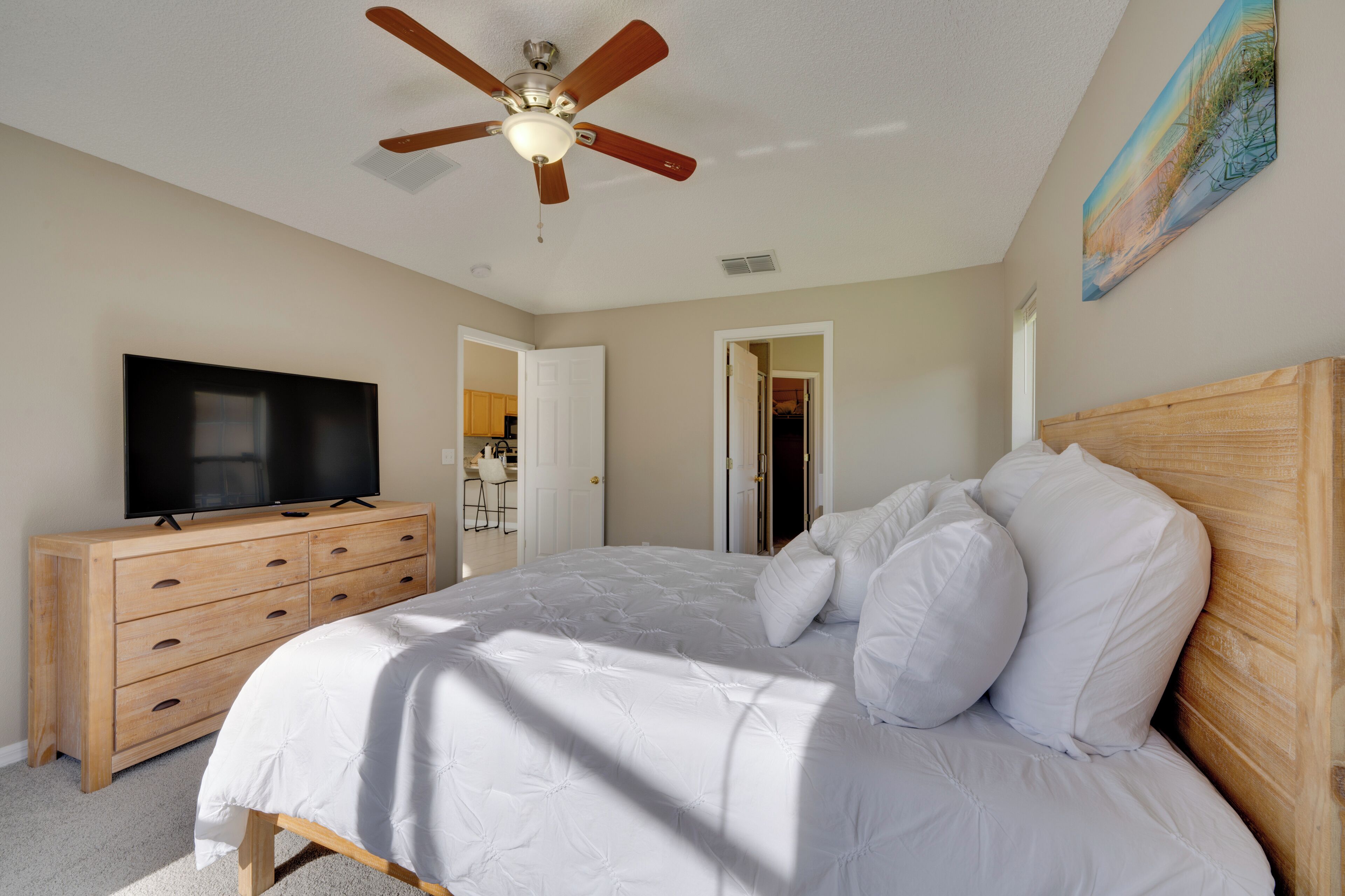 Ein Schlafzimmer mit einem Bett, einer Holzkommode, einem Deckenventilator und einem Fernseher.