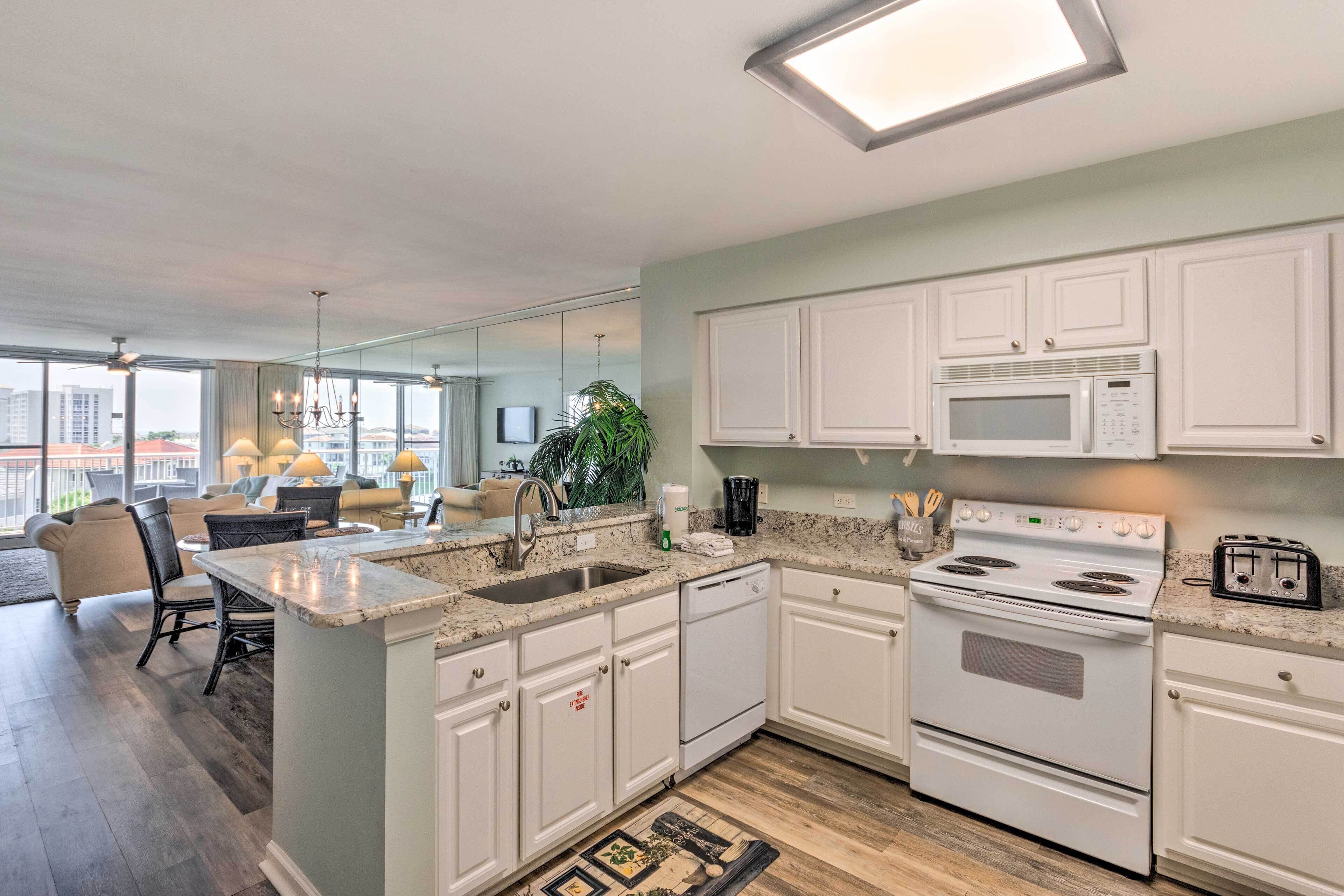 A modern kitchen with white cabinetry, a built-in microwave, and a stove. There is a dining area with a table and chairs, and a large window providing natural light.