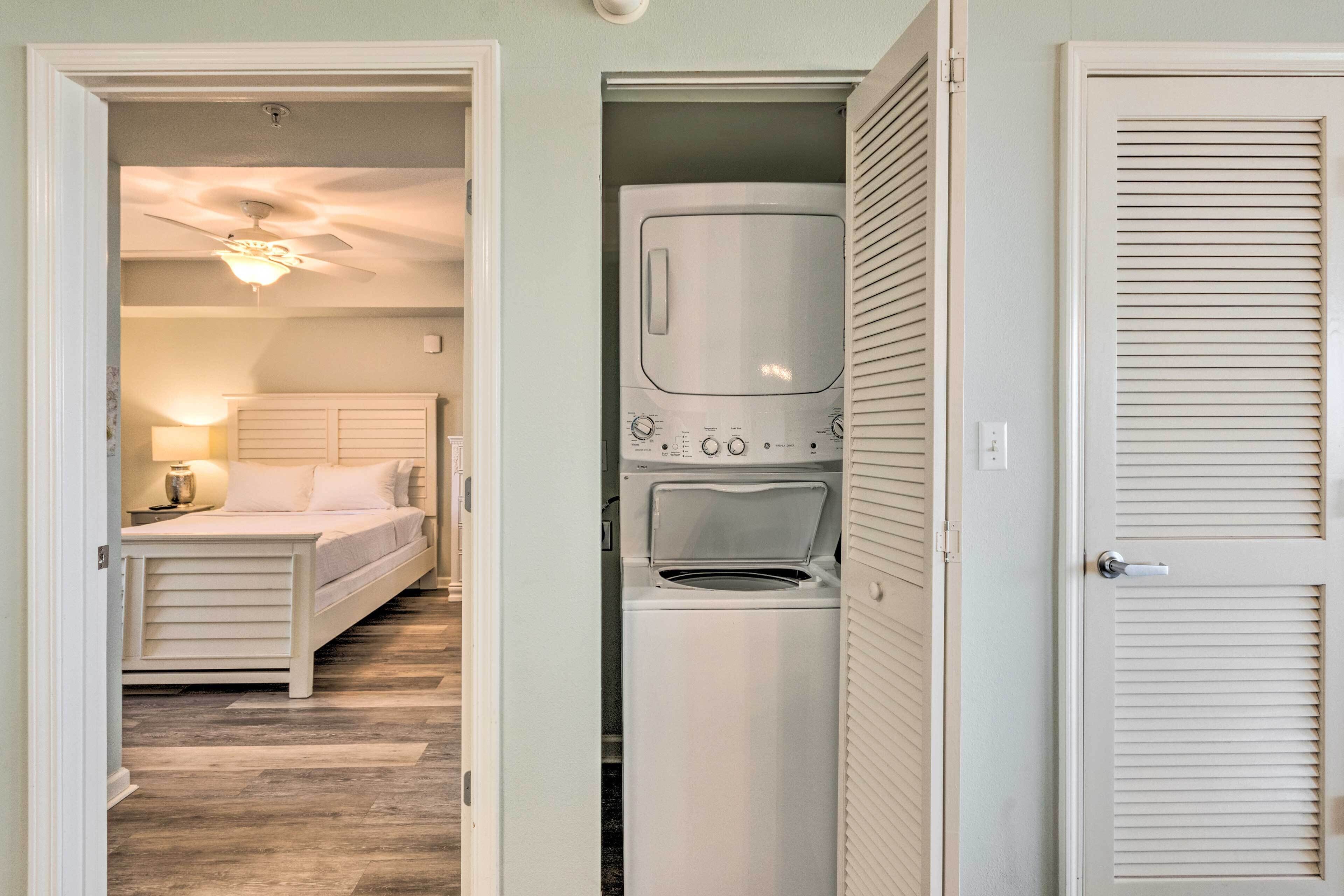 A compact room with a bed, a washing machine, and a ceiling fan.
