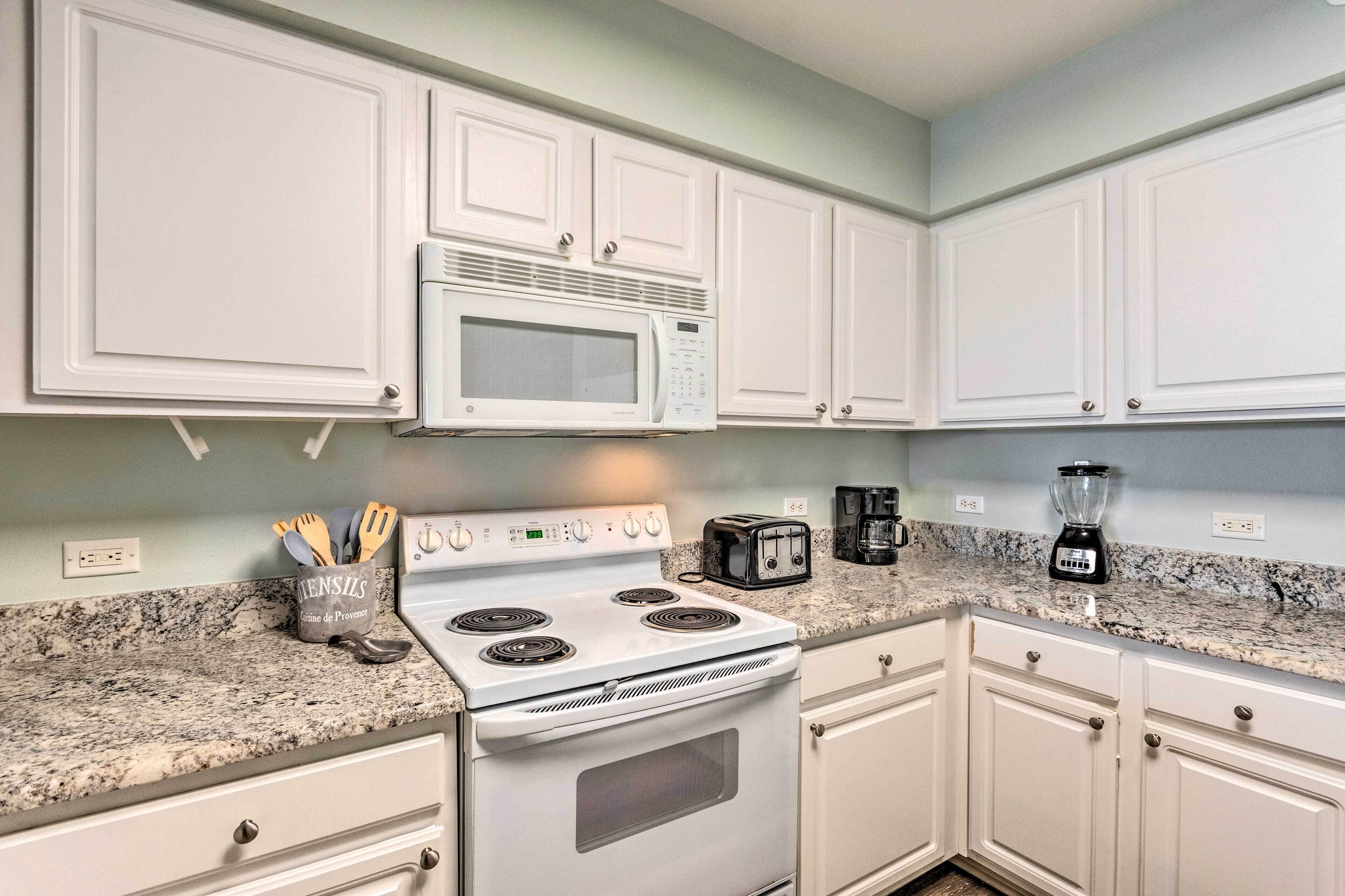 A kitchen with white cabinets, a white stove, a microwave, a toaster, a coffee maker, and a blender.
