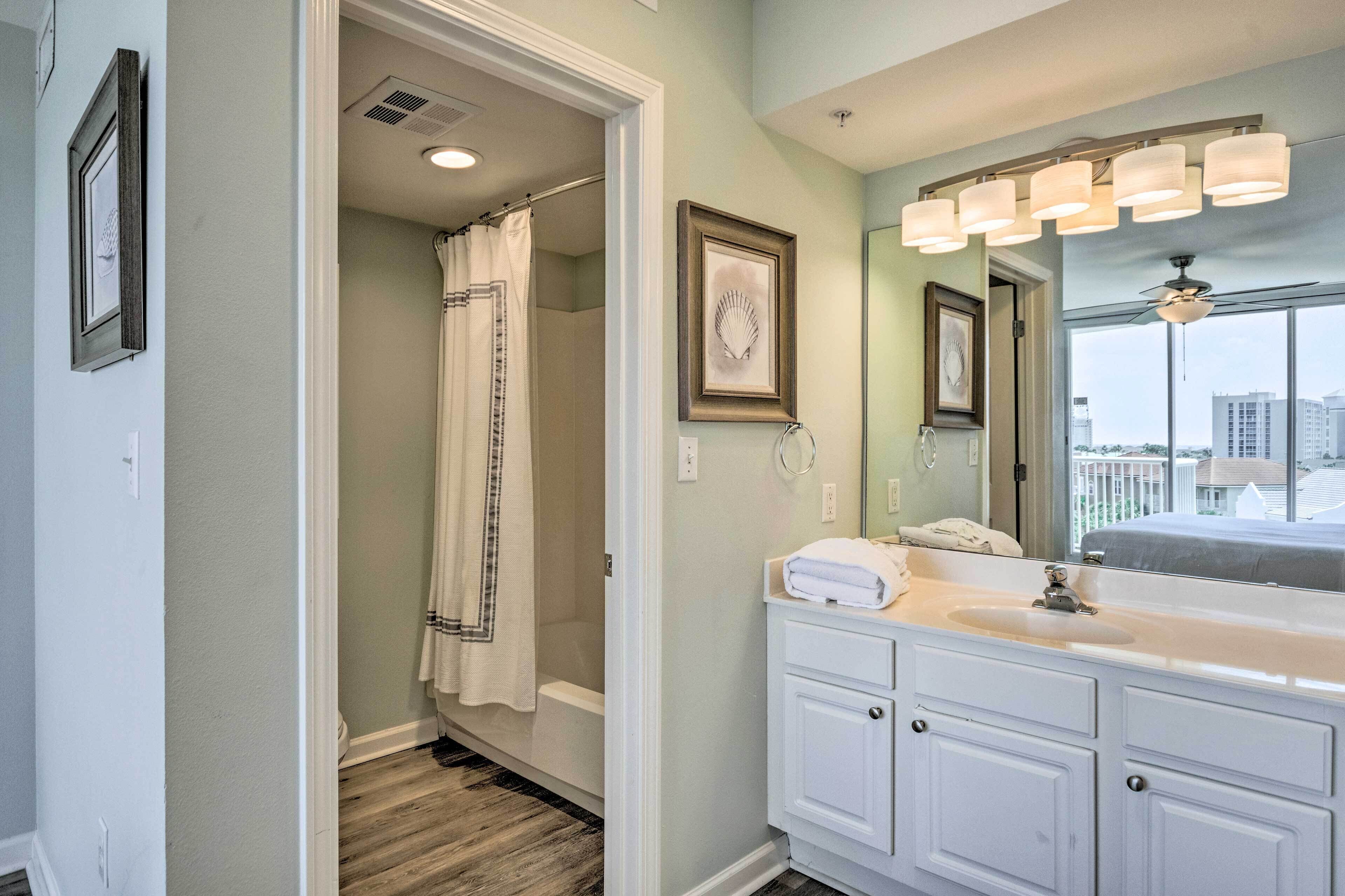 A bathroom with a walk-in shower, a large mirror with lights, and a view of buildings through the window.