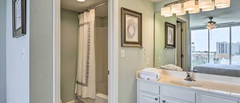 A bathroom with a walk-in shower, a large mirror with lights, and a view of buildings through the window.