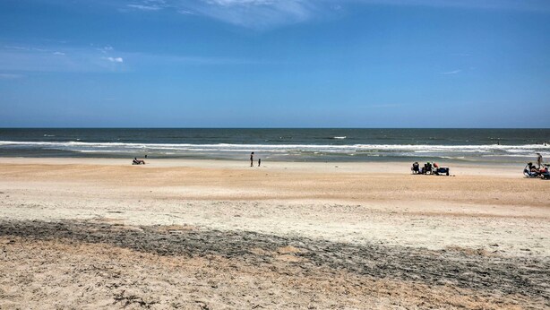 A beach with a clear sky, calm sea, and a few people and vehicles on the sand. - Beachfront Cottage in St Augustine - Pet Friendly! (St. Augustine)