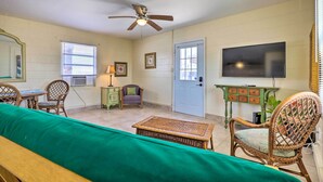 A living room with a ceiling fan, a television, wicker furniture, and a green sofa. - Beachfront Cottage in St Augustine - Pet Friendly! (St. Augustine)
