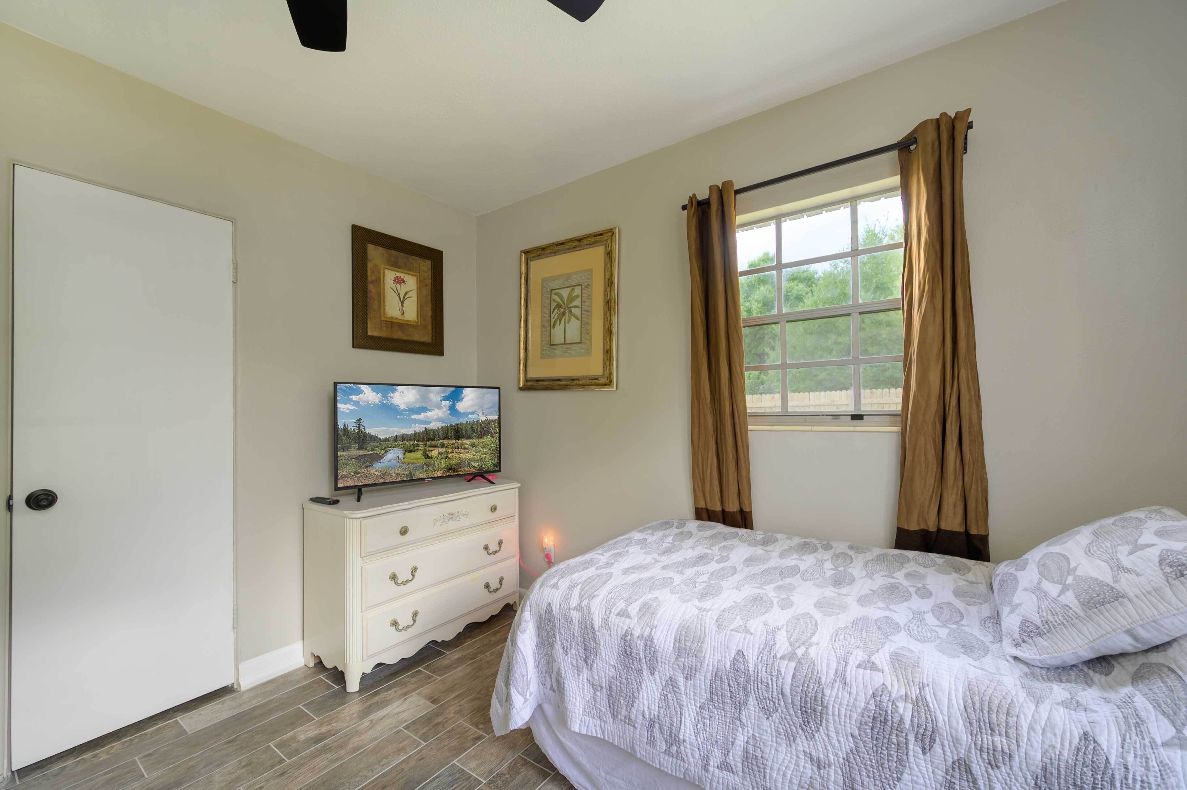 Une chambre à coucher comprenant un lit, une commode, un téléviseur et deux tableaux encadrés accrochés au mur.