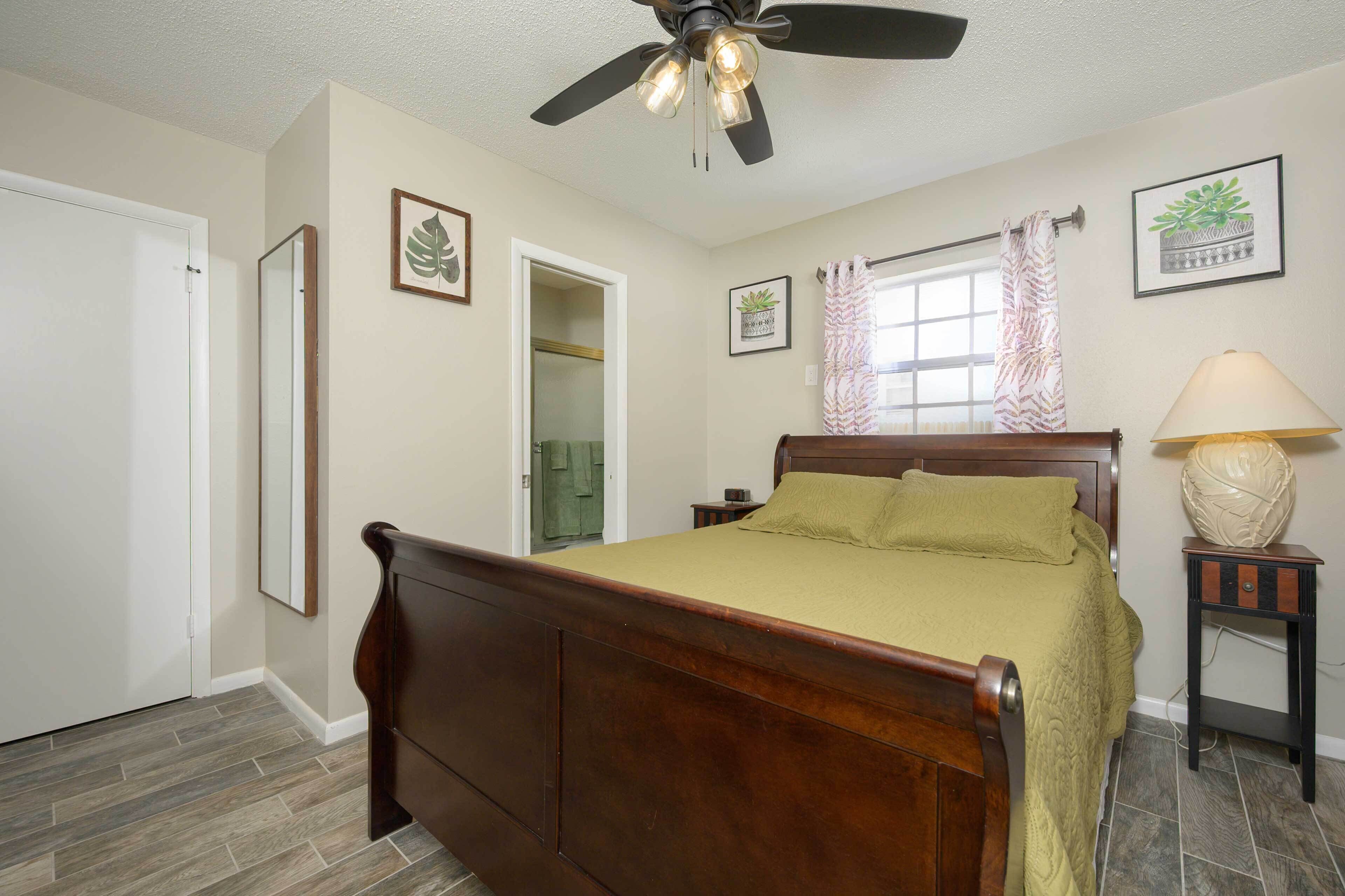 A bedroom with a wooden bed, a ceiling fan, a bedside table with a lamp, and a window with curtains.