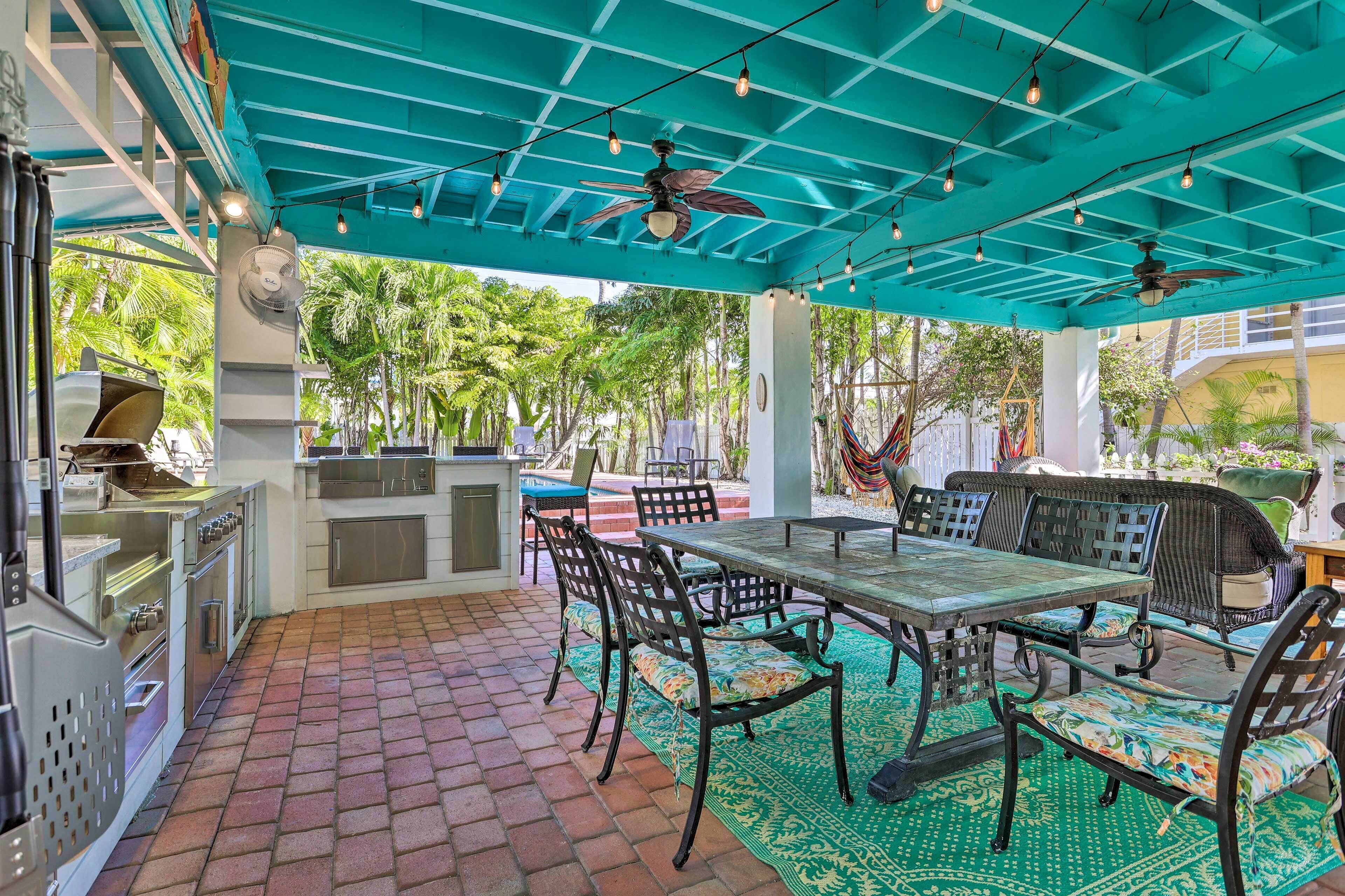 An outdoor patio with a table and chairs, a ceiling fan, and a brick floor.