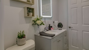 Casa de banho com lavatório branco, espelho, toalha e plantas em vasos.