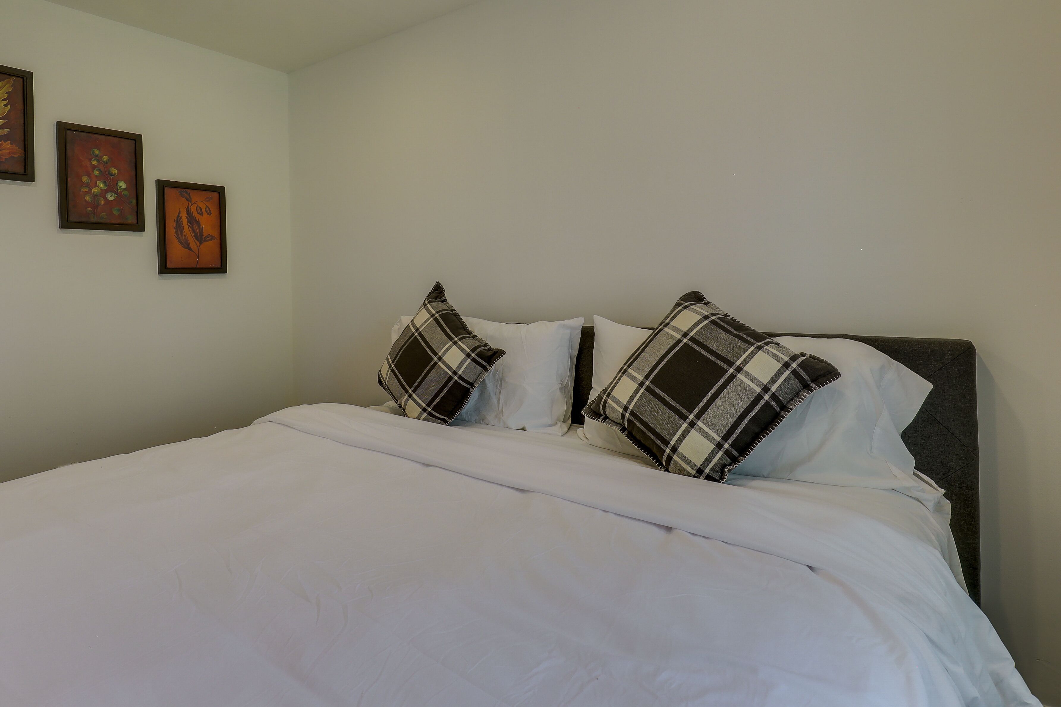 A neatly made bed with white bedding and two plaid pillows.