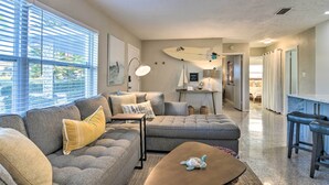 A modern living room with a sectional sofa, a coffee table, and a surfboard on the wall. - Lush Seminole Surf Inn w/ Backyard Fire Pit! (Seminole)