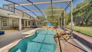 Une piscine avec un patio couvert, un panier de basketball et un mur en pierre.