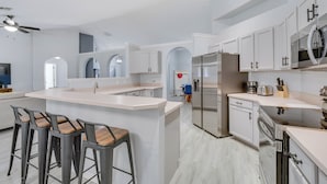 Une cuisine moderne avec des meubles blancs, un réfrigérateur en acier inoxydable et un coin bar équipé de tabourets.