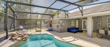 A covered outdoor swimming pool with lounge chairs, a blue sofa, and a patio area with a table and chairs.