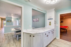 A kitchen with a marble countertop, white cabinets, and a red pool table in the adjacent room. - Indialantic Oasis - 2 Mi to Canova Beach Park (Indialantic)