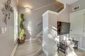 Una escalera con acabado de madera, una lámpara de pared y una planta decorativa.