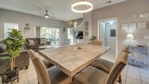 A spacious living room with a large dining table, comfortable seating, and a ceiling fan.