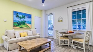 A living room with a sofa, coffee table, dining table with chairs, a painting on the wall, and a window with curtains. - 3 Mi to Disney: Home w/ Hot Tub in Margaritaville! (Kissimmee)