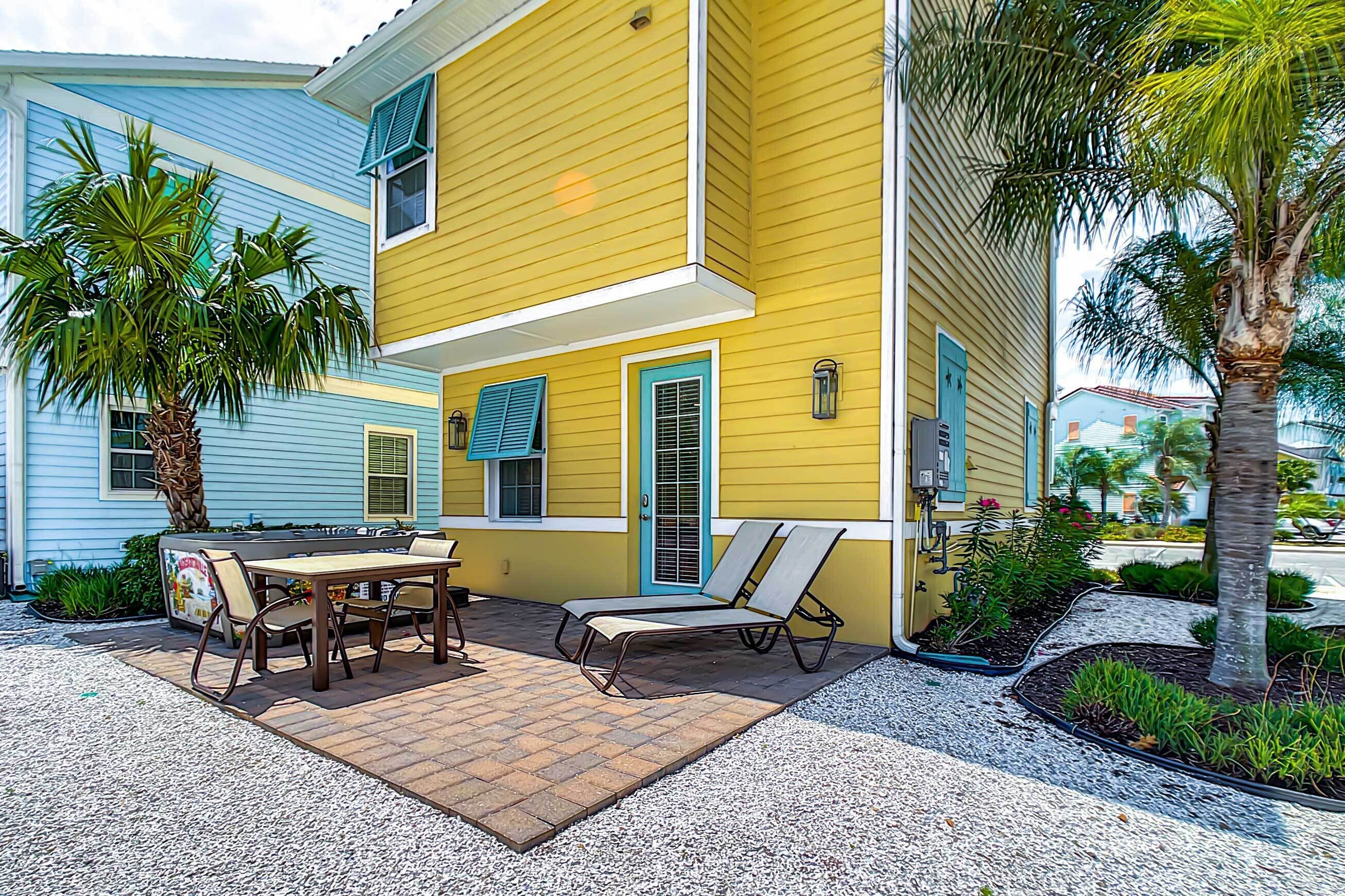 A two-story yellow house with a patio, outdoor furniture, and a palm tree.