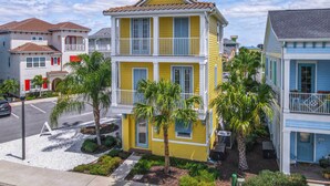 A multi-story yellow building with balconies, surrounded by palm trees and other residential structures. - 3 Mi to Disney: Home w/ Hot Tub in Margaritaville! (Kissimmee)