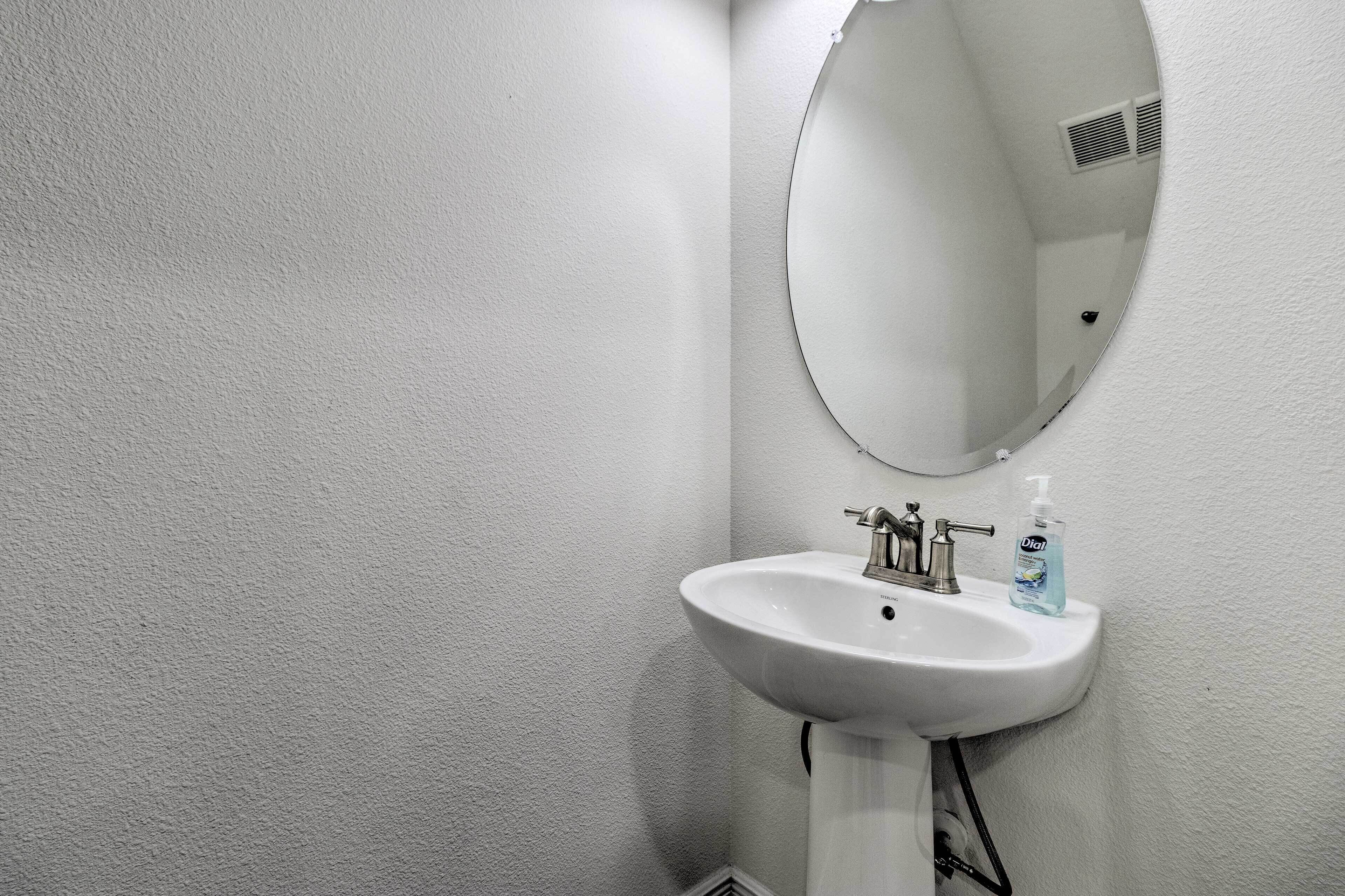 A white bathroom with a round mirror, a white sink, and a bottle of hand soap.