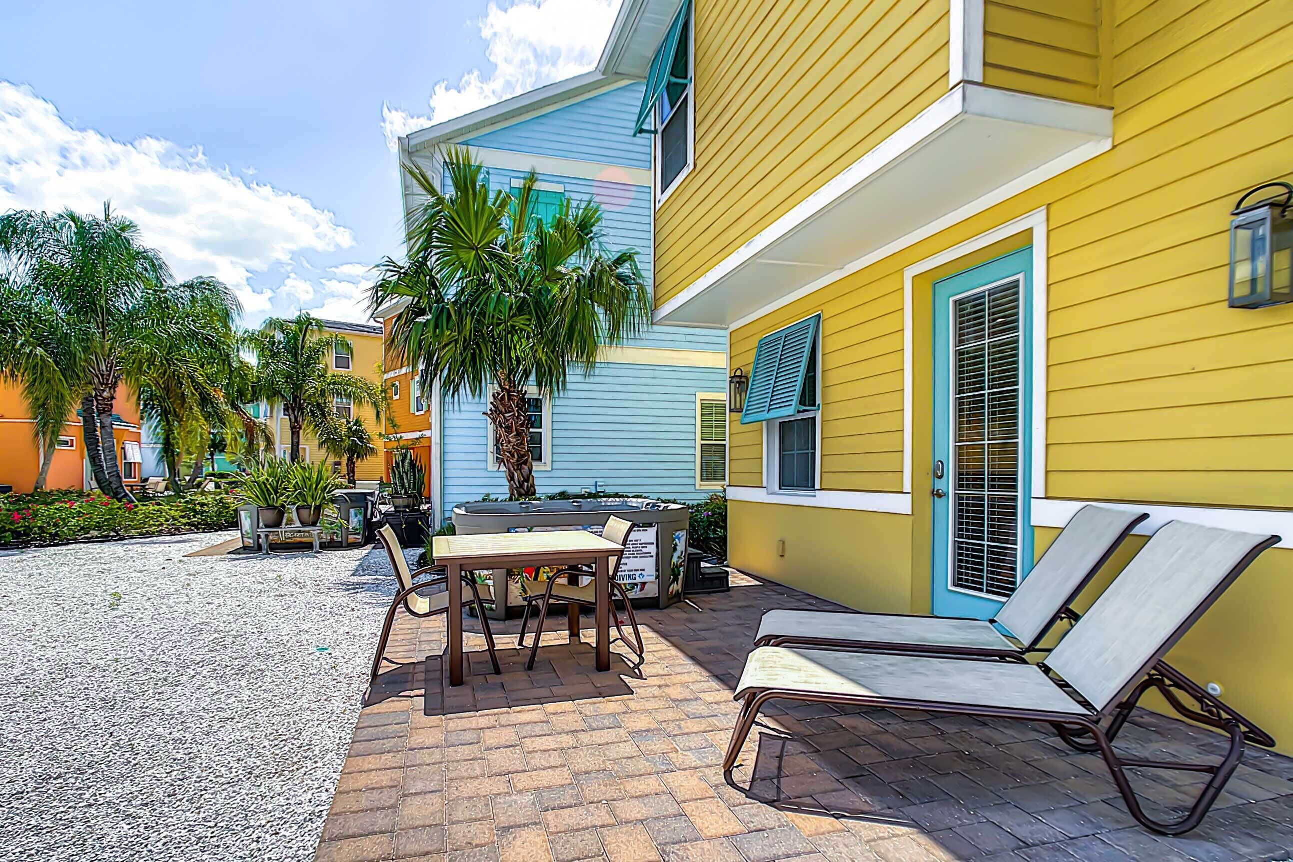 A courtyard with a table and chairs, a lounge chair, and a palm tree.