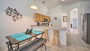 A modern kitchen with wooden cabinets, a central island, bar stools, and a dining table with blue placemats. - Pool + Lanai: Emerald Isle Resort Home! (Kissimmee)