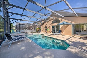 A pool area with a glass enclosure, lounge chairs, and a patio area with a table and chairs. - Pool + Lanai: Emerald Isle Resort Home! (Kissimmee)