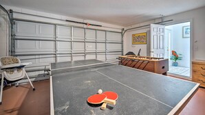 A ping pong table in a room with a garage door, a foosball table, and a chair. - Pool + Lanai: Emerald Isle Resort Home! (Kissimmee)