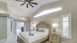 A bedroom with a large bed, a nightstand, a ceiling fan, and a window with blinds. - Luxe Waterfront Oasis w/ Dock, Heated Pool & Spa! (Port Charlotte)