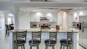 A modern kitchen with white cabinets, a central island with bar stools, stainless steel appliances, and recessed ceiling lighting. - Luxe Waterfront Oasis w/ Dock, Heated Pool & Spa! (Port Charlotte)