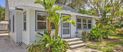 A single-story house with a front porch, large windows, and a small garden with tropical plants.